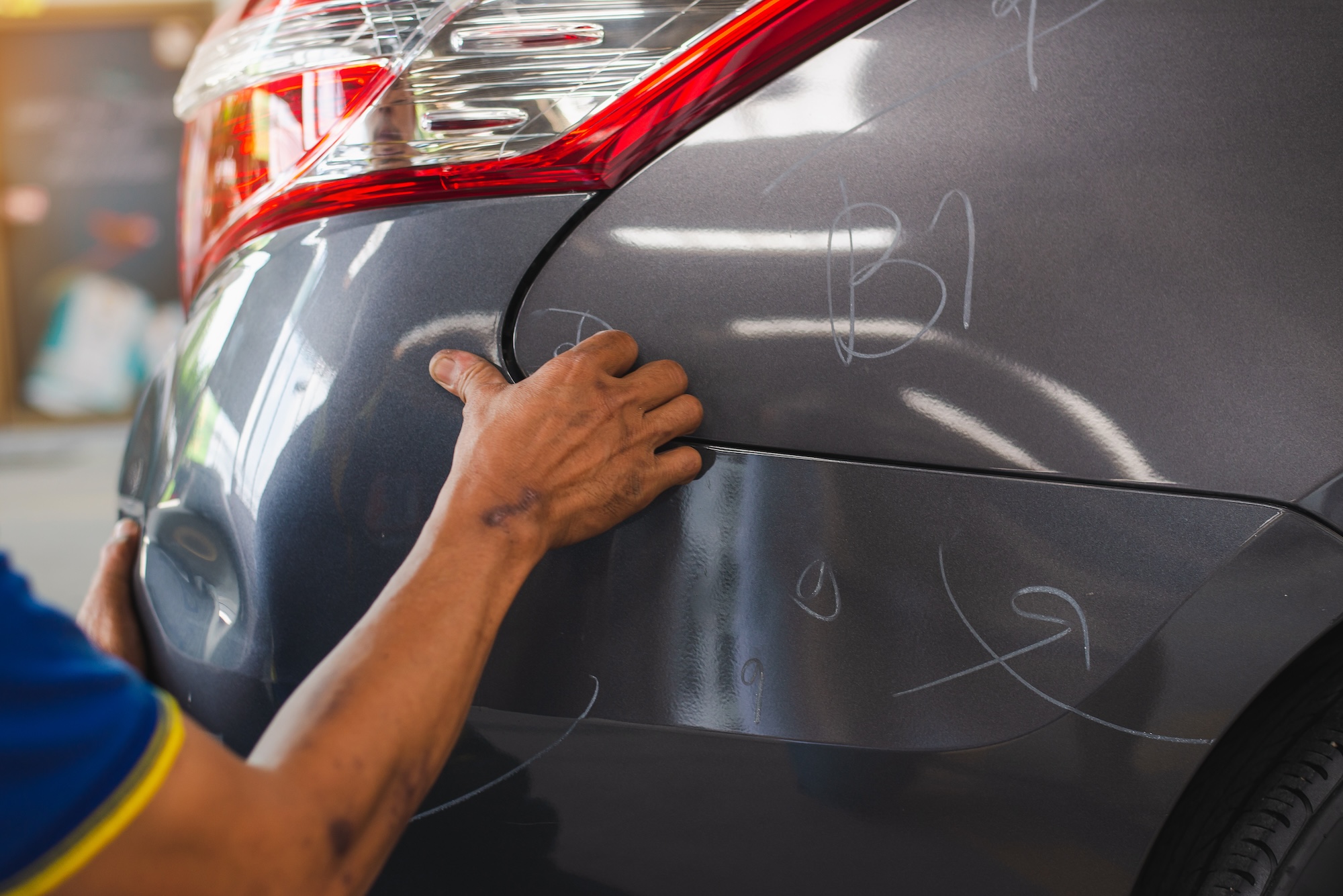 Auto technician aligning a car’s rear panel during bumper repair at a professional collision center in Miami.